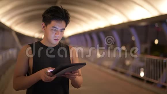 年轻英俊的亚洲男子夜间在户外使用数码平板电脑时思考的肖像视频的预览图