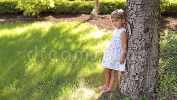 公园里一个色彩斑斓的可爱小女孩靠着一棵大树站着视频的预览图