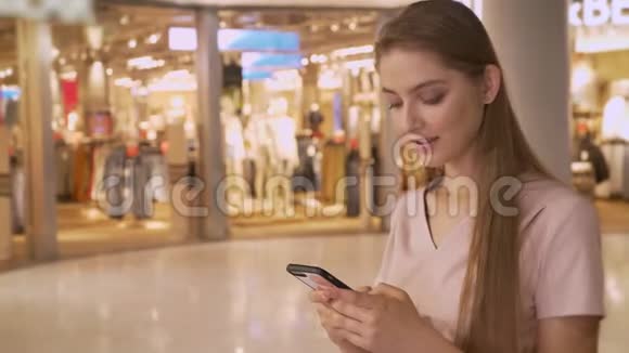 年轻迷人的女孩去购物中心购物智能手机聊天看相机购物理念时尚视频的预览图