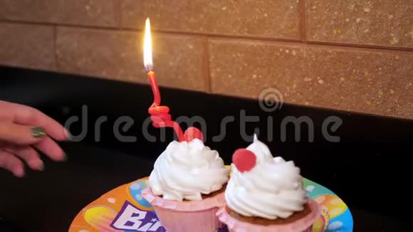 特写镜头在一个节日的盘子里两个漂亮的带白色奶油和浆果的纸杯蛋糕一根蜡烛在一根视频的预览图