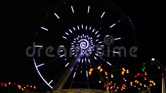 摩天轮在夜晚运行灯光照亮大旋转木马上五颜六色的运行灯视频的预览图
