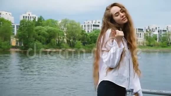 快乐的年轻女人穿着白色衬衫长发戴着耳机跳舞欧洲迷人的女孩听音乐视频的预览图