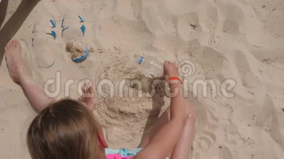 金发孩子倒水在海滩上用沙子做蛋糕俯视风景视频的预览图