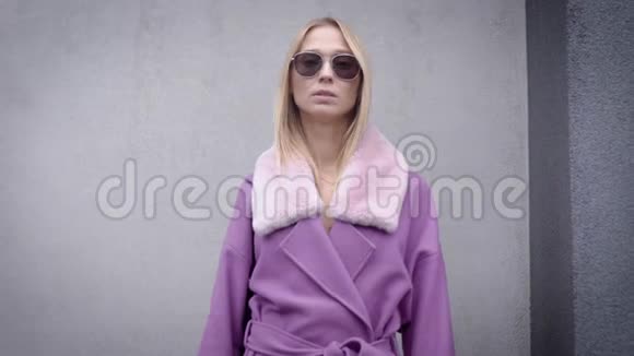 一个穿着紫色外套和太阳镜的迷人金发女孩的肖像寒冷的秋天天气视频的预览图