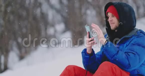 一位坐在雪地上的男性滑雪者通过电话为社交网络拍摄一处美丽的度假胜地景观视频的预览图