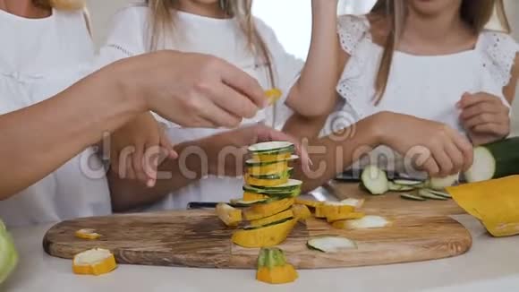 一位美丽的母亲和两个穿着白色衣服的孩子在厨房里做了一个由黄色和绿色的西葫芦组成的金字塔视频的预览图