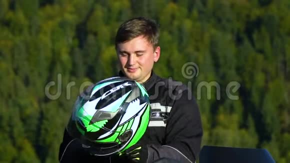一个骑摩托车的人带着摩托车在山上的年轻帅哥特写镜头他戴着头盔慢慢视频的预览图