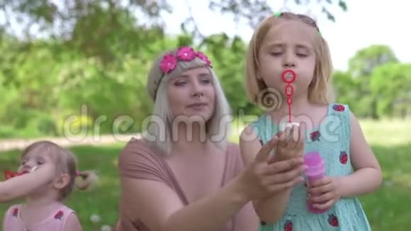 年轻的金发嬉皮士妈妈在公园里和她的小女孩一起吹肥皂泡女儿们穿视频的预览图