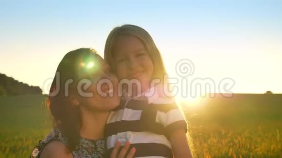 迷人的年轻母亲拥抱着她的金发小女儿看着镜头微笑着日落时的麦田视频的预览图
