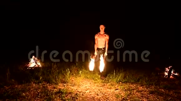 低调一个留着长发和赤裸躯干的年轻男性在黑色的夜晚缓慢地旋转着燃烧的火炬视频的预览图