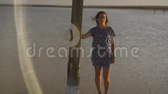 苗条的女孩欣赏日落站在盐湖的一根木盐柱附近视频的预览图
