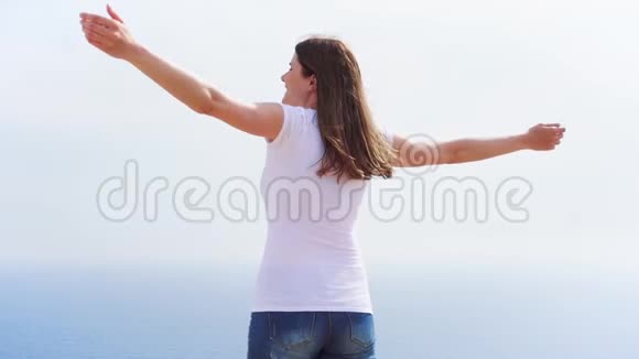 微笑的女人在悬崖上与蓝色的大海搏斗无忧无虑的女电车慢动作视频的预览图