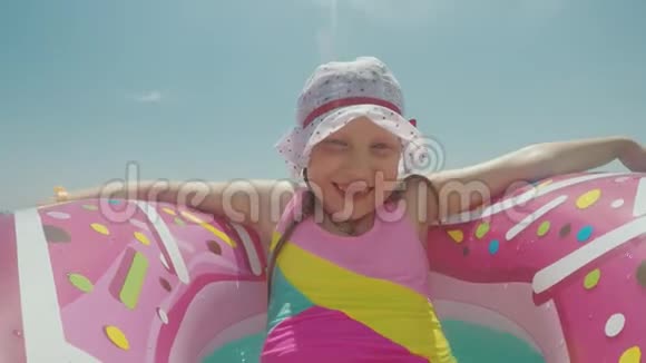 一个戴着粉色充气戒指的有趣女孩穿着一件有趣的儿童服装在阳光下晒太阳在海浪上打滚视频的预览图