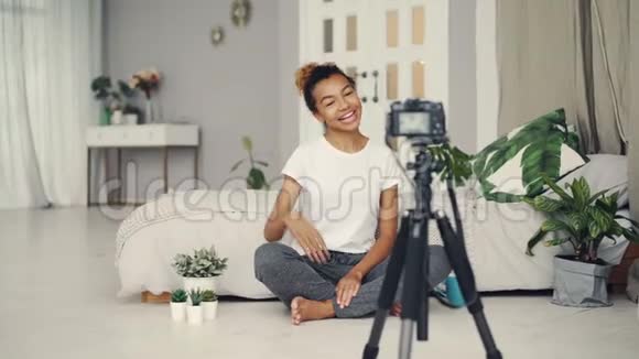 漂亮的非裔美国女孩创意博客作者正在录制关于坐在公寓地板上的植物的视频视频的预览图