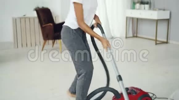 活跃的女家庭主妇正在用吸尘器打扫房间用耳机听音乐跳舞和视频的预览图