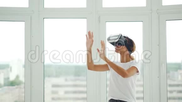 穿休闲服装的非裔美国女孩站在自己的公寓里用虚拟现实眼镜和手势视频的预览图