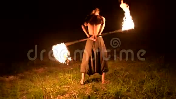 低调一个留着长发和赤裸躯干的年轻男性在黑色的夜晚缓慢地旋转着燃烧的火炬视频的预览图