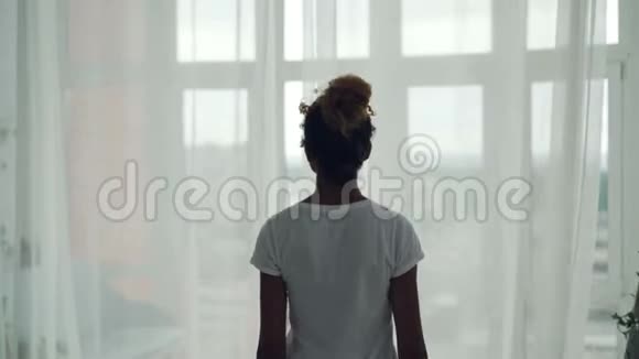 年轻的非洲裔美国女孩正走到家中的窗户前拉开窗帘然后从窗户欣赏风景视频的预览图