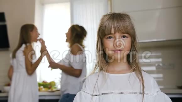 英俊的小女孩吃着大绿苹果她的妈妈和姐姐在厨房的背景下准备食物视频的预览图