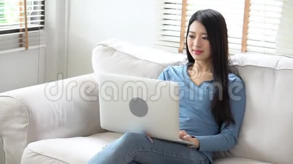 美丽的亚洲年轻女子坐在沙发上用笔记本电脑显示视频通话在家聊天视频的预览图