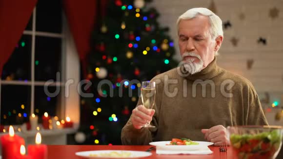 孤独的男人坐在闪闪发光的圣诞树旁在圣诞前夜喝着香槟视频的预览图