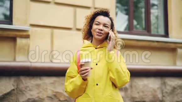 粗心的非裔美国女孩正在现代城市的户外打电话拿着外卖咖啡视频的预览图