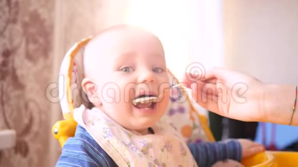 小可爱的宝宝看着镜头妈妈用勺子喂他在高椅子上慢慢地视频的预览图