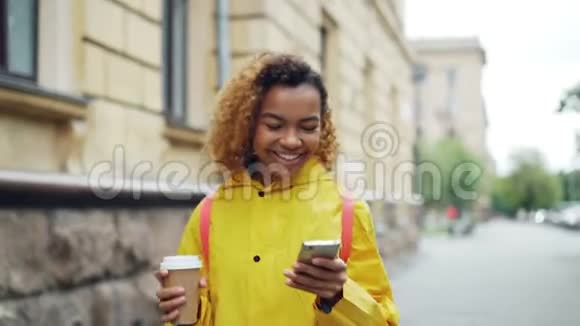 快乐的非洲裔美国妇女使用智能手机触摸屏幕微笑着在美丽的城市户外散步视频的预览图