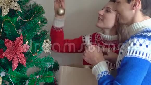 年轻夫妇在家装饰圣诞树穿冬天毛衣的人视频的预览图