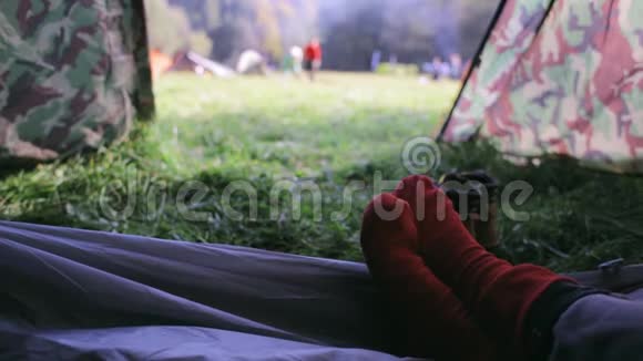 在露营地的帐篷里第一个人可以看到穿着红袜子的女人的腿和在松树林里的绿草上的帐篷视频的预览图