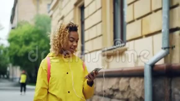 漂亮的非裔美国女士正在听收音机戴着耳机拿着现代智能手机女孩是视频的预览图