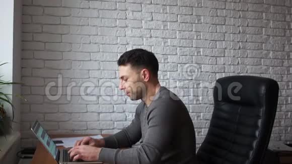 英俊的商人在办公室里用笔记本电脑工作一个男人坐在皮椅上靠在白色砖墙上视频的预览图