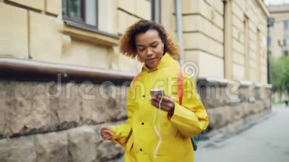 年轻的非洲裔美国妇女正通过耳机听音乐并在现代城市沿街跳舞视频的预览图