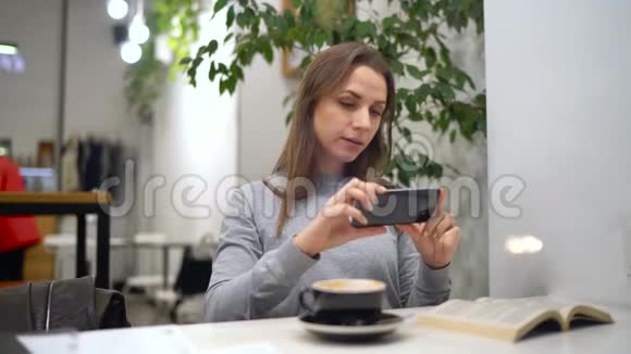 美女在咖啡馆为社交网络拍照咖啡和书籍视频的预览图
