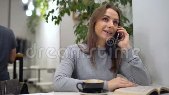 美丽的女人把时间花在咖啡馆里看书打电话喝咖啡视频的预览图