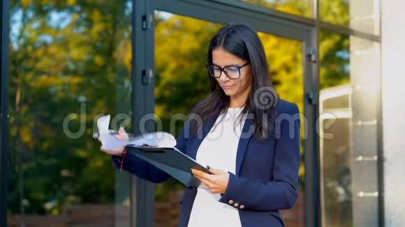 年轻漂亮的黑发女人穿西装戴眼镜检查文件公用事业账单报告女商人站在附近视频的预览图