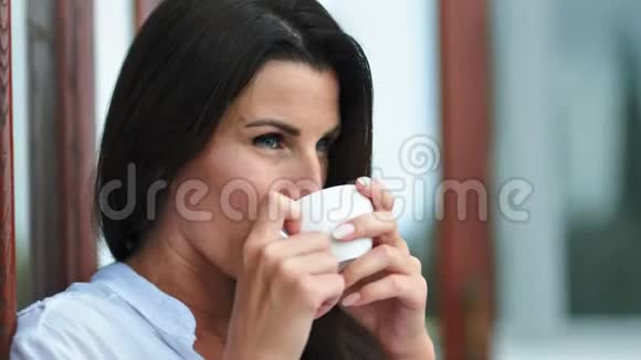 快乐的女性脸喝着咖啡或茶手捧着白瓷杯享受周末视频的预览图