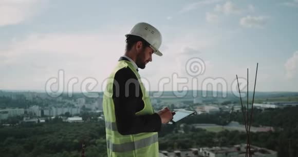 年轻的商人站在建筑工地的顶端用平板电脑分析建筑视频的预览图