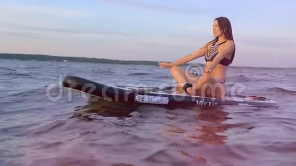 年轻漂亮的女士坐在桨板上摆出一个莲花的姿势视频的预览图