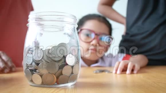 一个亚洲小女孩带着家庭母亲和大母亲把钱币放进透明的玻璃瓶里为教育理念省钱视频的预览图