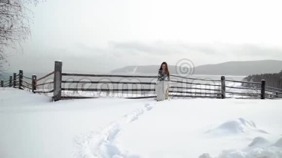 一个留着长发的少数民族女孩偷偷地从漂流中溜走背景中是木栅栏和山脉下雪视频的预览图