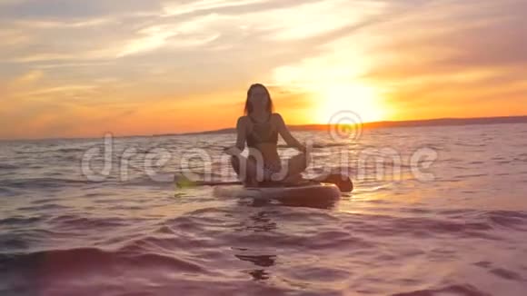在夕阳下练习瑜伽的时候漂亮的女人正坐在一个莲花的姿势上视频的预览图