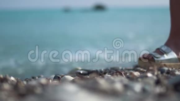 时尚女性银色拍打人字拖鞋特写高跟鞋踩在碧海背景的鹅卵石上视频的预览图