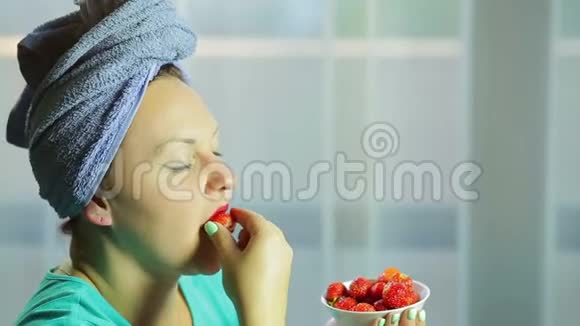 一个头上戴毛巾的年轻女人把草莓放进嘴里吃我视频的预览图