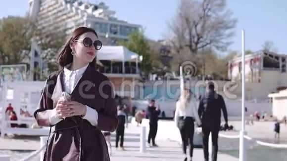 可爱时尚的黑发女孩走在码头附近的海洋和吃冰淇淋在阳光明媚的一天视频的预览图