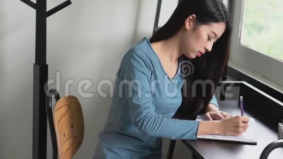 美丽的亚洲年轻女子手在桌上的笔记本上写字女孩在家写书或日记视频的预览图