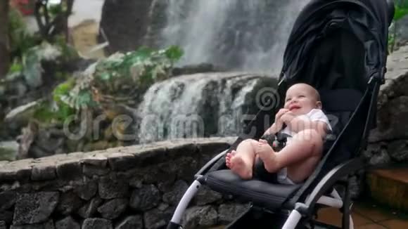 婴儿坐在瀑布附近的轮椅上笑着看着相机在remsa和父母一起旅行视频的预览图