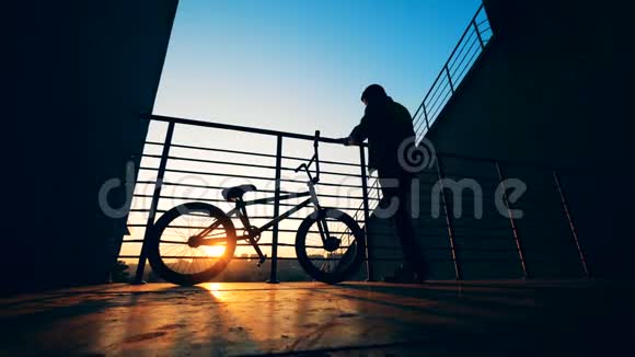 在日落时分一个男孩骑着自行车站在站台上头发乱成一团视频的预览图