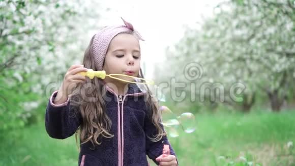 小女孩在盛开的花园里玩肥皂泡慢动作视频的预览图