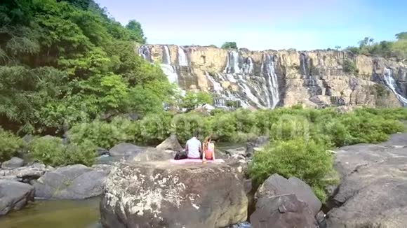坐在岩石手表瀑布旁边的男人女孩视频的预览图